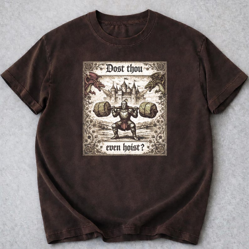 May include: Brown t-shirt with a medieval-themed illustration. The design shows a knight lifting weights, accompanied by the text "Dost thou even hoist?". The artwork includes dragons and a castle, creating a vintage aesthetic.