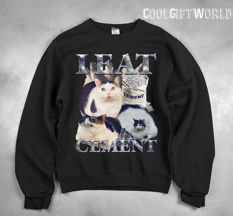 Pode incluir: Camisola preta com um gr&aacute;fico de quatro gatos e um saco de cimento. O texto "EAT CEMENT" &eacute; exibido em letras met&aacute;licas acima e abaixo dos gatos. A camisola tem gola redonda e mangas compridas.