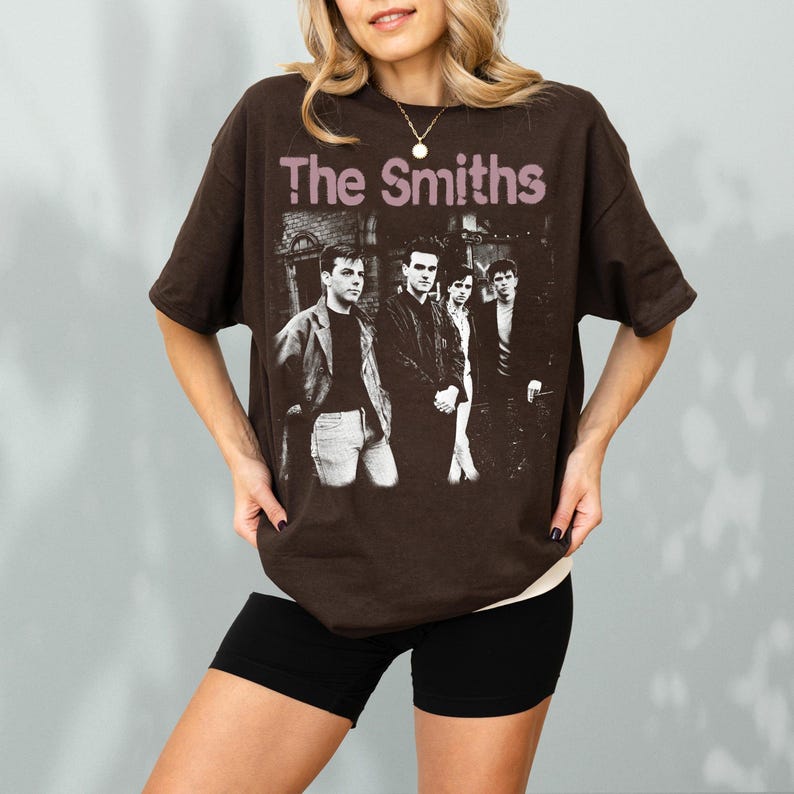 May include: A brown t-shirt featuring the band "The Smiths" with a black and white image of the band members. The band's name is printed in a light purple color across the top of the image.