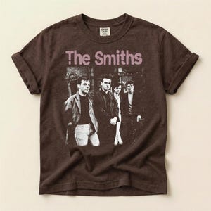 May include: Brown t-shirt featuring the band "The Smiths" with a black and white image of the band members. The band's name is printed in a light purple color across the top of the image.