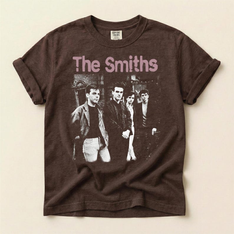 May include: Brown t-shirt featuring the band "The Smiths" with a black and white image of the band members. The band's name is printed in a light purple color across the top of the image.