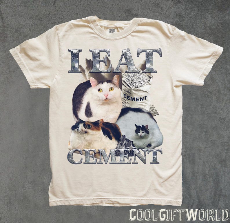 Pode incluir: Camiseta creme com um gr&aacute;fico de tr&ecirc;s gatos e um saco de cimento. O texto "I EAT CEMENT" &eacute; impresso acima e abaixo dos gatos em uma fonte met&aacute;lica. A camiseta tem mangas curtas.