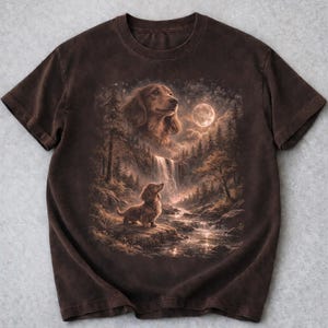 May include: Brown t-shirt with a detailed illustration of a dachshund dog in a forest scene with a waterfall, a full moon, and trees. The artwork has a vintage, painterly style.