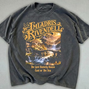 Könnte beinhalten: Dunkelgraues T-Shirt mit dem goldenen Schriftzug "Imladris Rivendell" über einer Landschaft mit Wasserfällen und einer Brücke. Der Text "The Last Homely House East of the Sea" steht darunter. Rundhalsausschnitt und kurze Ärmel.