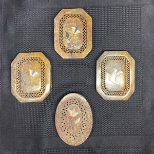 Peut inclure: Quatre pièces décoratives en pierre avec incrustation florale. Trois sont rectangulaires avec une bordure en treillis, et une est ovale. L'incrustation présente des motifs floraux blancs, gris et rouges. La pierre a une teinte chaude et terreuse.
