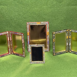 Puede incluir: Una colección de marcos de fotos decorativos con bordes de mosaico coloridos. Los marcos son de varios tamaños y configuraciones, incluyendo diseños de panel simple y doble. Los marcos tienen interiores dorados y negros, sobre un fondo verde.