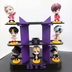 May include: A black and purple display shelf with seven small figurines. The figurines are of cartoon characters with different hair colors and outfits. The shelf has the letters "BTS" on the front.