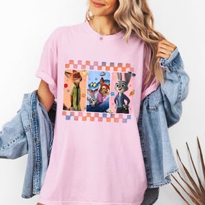 Może przedstawiać: Jasnor&oacute;żowa koszulka z kolorową grafiką postaci z animowanego filmu Zwierzogr&oacute;d. Grafika jest obramowana wzorem w kratę. Koszulka ma swobodny, obszerny kr&oacute;j.