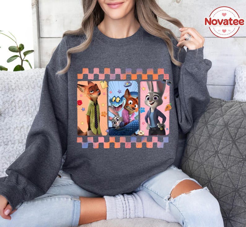 Może przedstawiać: Ciemnoszara bluza z kolorową grafiką postaci z filmu animowanego Zwierzogr&oacute;d. Grafika zawiera Nicka Wilde'a, Judy Hopps i inne postacie w obramowanej kompozycji. Bluza ma długie rękawy i okrągły dekolt.