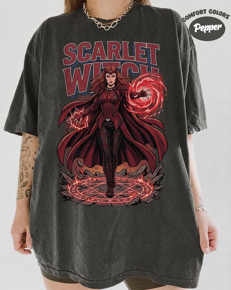 May include: A charcoal grey t-shirt featuring a graphic of the Scarlet Witch in a red costume with a flowing cape, surrounded by red magical energy and a glowing circular rune on the ground. The text "SCARLET WITCH" is printed above in red.