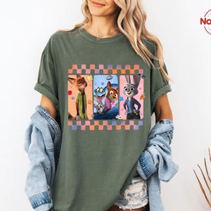 Może przedstawiać: Zielona koszulka z nadrukiem postaci z animowanego filmu Zwierzogr&oacute;d. Grafika jest obramowana wzorem w kratkę w kolorze r&oacute;żowym, pomarańczowym i fioletowym. Koszulka ma kr&oacute;tkie rękawy i luźny kr&oacute;j.