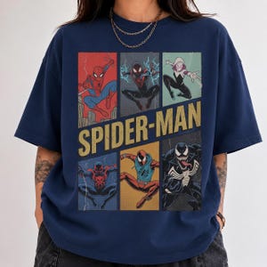 May include: A navy blue t-shirt featuring a graphic print of various Spider-Man characters in a comic book panel layout. The text SPIDER-MAN is printed in large yellow letters across the centre of the design, surrounded by illustrations of different heroes.