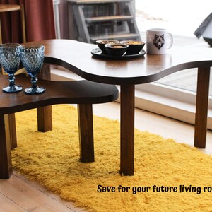 May include: Two wooden coffee tables with a unique, organic shape. The top table has a wavy edge and the bottom table has a more rounded shape. Both tables have a dark brown finish and are sitting on a yellow shag rug.