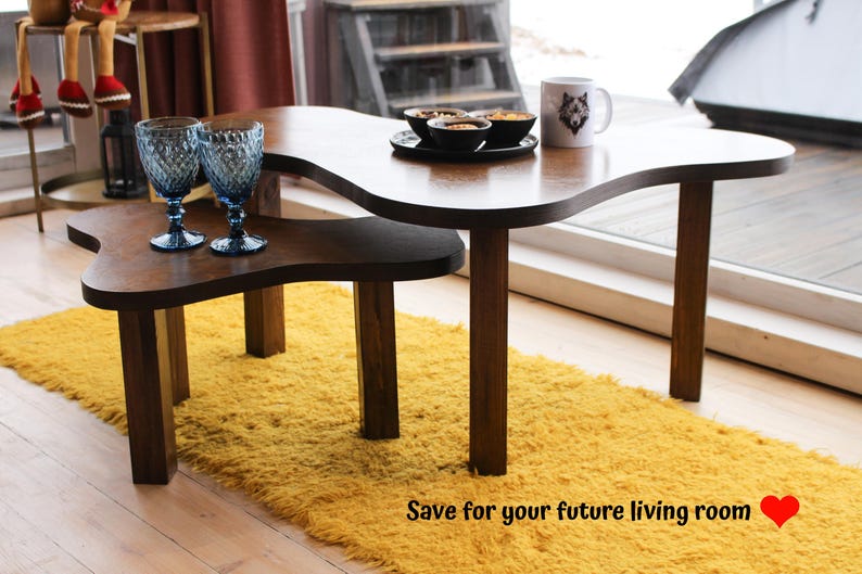 May include: Two wooden coffee tables with a unique, organic shape. The top table has a wavy edge and the bottom table has a more rounded shape. Both tables have a dark brown finish and are sitting on a yellow shag rug.