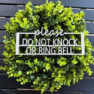 Puede incluir: Una corona redonda de eucalipto artificial verde con un letrero blanco que dice "please DO NOT KNOCK OR RING BELL". El letrero es rectangular y está centrado en la corona.