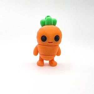May include: A 3D-printed orange carrot character with a green leafy top. The figure has large black eyes, a small smile, and tiny arms and legs. The whimsical design is set against a white background.