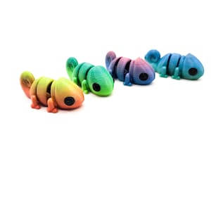 Op de afbeelding: Vier kleurrijke, gesegmenteerde kameleon speelgoed in tinten oranje, groen, blauw en paars. Elke kameleon heeft een zwart oog en staat op een witte achtergrond. Het speelgoed lijkt 3D-geprint.