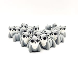 Puede incluir: Una colección de gomas de borrar grises con forma de oso, con ojos negros y caras blancas. Las gomas están dispuestas juntas sobre un fondo blanco, creando una estética lúdica. Los osos tienen un diseño lindo y de dibujos animados.