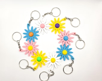 Peut inclure: Plusieurs porte-clés en forme de marguerite de différentes couleurs, dont le bleu, le rose, le jaune et le blanc. Chaque porte-clés est doté d'une chaîne et d'un anneau argentés. Les centres des marguerites sont également de couleurs variées.