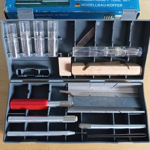 May include: Open grey plastic hobby craft tool set containing various tools, including blades, handles, and small containers. The set includes a red-handled tool and a blue box with text.