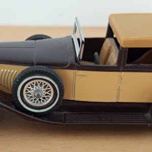 May include: A vintage model car in shades of brown and tan. The car features a convertible top, detailed wheels, and chrome accents. The classic design evokes a sense of nostalgia and automotive history.