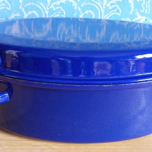 Peut inclure: Un plat à casserole en émail bleu cobalt avec un couvercle. Le plat rond a deux poignées en boucle et un couvercle assorti. L'ustensile de cuisine est en métal et convient à la cuisson. Le plat mesure environ 25 cm de diamètre.