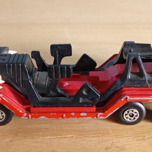 Op de afbeelding: Een vintage rode en zwarte speelgoedvrachtwagen met zes wielen. De speelgoedvrachtwagen heeft een ontwerp met een laadvloer met zwarte structuren en een rode cabine. De achterkant van de vrachtwagen heeft de tekst "X4" in het wit.