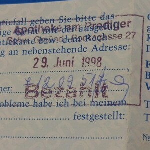 Puede incluir: Primer plano de un documento antiguo con texto y sellos en alem&aacute;n. El documento incluye la fecha "29. Juni 1998" y la palabra "Bezahlt" estampada en tinta p&uacute;rpura. El papel est&aacute; ligeramente envejecido con un fondo azul.