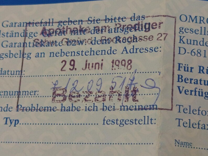 Puede incluir: Primer plano de un documento antiguo con texto y sellos en alem&aacute;n. El documento incluye la fecha "29. Juni 1998" y la palabra "Bezahlt" estampada en tinta p&uacute;rpura. El papel est&aacute; ligeramente envejecido con un fondo azul.