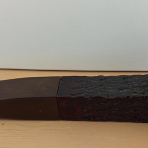 Könnte beinhalten: Eine dunkelbraune Tabakpfeife mit einem strukturierten Kopf und einem glatten, abgewinkelten Mundstück. Die Pfeife besteht aus einem dunklen Material, möglicherweise Holz, und ist zum Rauchen bestimmt. Der Kopf hat eine weite Öffnung, und das Mundstück ist lang und schlank.