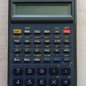 Puede incluir: Calculadora científica Sharp EL-531GH verde oscuro con pantalla de funciones. La calculadora tiene numerosos botones para funciones matemáticas, incluidos cálculos trigonométricos, logarítmicos y estadísticos. La calculadora es rectangular.