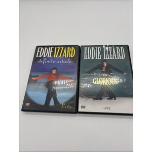 Peut inclure: Deux boîtiers de DVD avec Eddie Izzard. Le boîtier de gauche est intitulé "definite article" avec une photo d'Izzard en veste rouge. Le boîtier de droite est intitulé "Glorious" avec Izzard en costume noir. Les deux boîtiers ont le mot "Live".