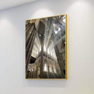May include: A framed print of a cathedral interior. The image captures the architectural details of the building, including tall columns, arched ceilings, and sunlight streaming through the windows. The frame is gold.