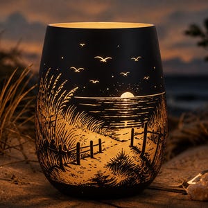 Könnte beinhalten: Ein zylindrischer schwarzer Kerzenhalter mit einem Scherenschnitt-Design einer Küstenlandschaft bei Sonnenuntergang. Die Silhouette zeigt einen Sandweg zum Meer, hohes Dünengras, einen Holzzaun und Vögel unter einer leuchtenden Sonne.