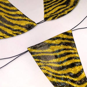 May include: A two-piece bikini set featuring a vibrant yellow and black tiger stripe pattern. The fabric has a shimmering, reflective finish. The top consists of two triangular cups, and the bottom is a triangular piece, both connected by thin black strings.
