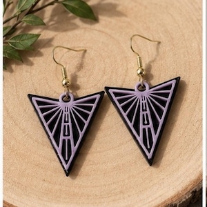 May include: A pair of black and lavender geometric earrings. Each earring is a triangle shape with a lavender interior design and gold-colored ear hooks. The earrings are displayed on a wooden surface.