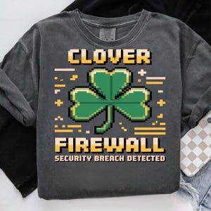 Può includere: Felpa grigio scuro con un design a trifoglio verde pixelato. Il testo "CLOVER FIREWALL SECURITY BREACH DETECTED" è stampato in giallo. La felpa ha maniche lunghe e girocollo.