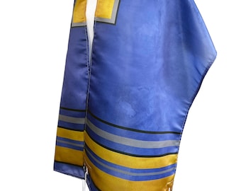 Può includere: Un tallit blu con strisce dorate e grigie e testo ebraico. Il tallit è fatto di raso e ha frange.