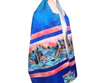 Può includere: Un tallit blu e rosa, scialle di preghiera ebraico, con un colorato design paesaggistico. Lo scialle presenta uno sfondo blu vibrante con strisce rosa e un'illustrazione dettagliata di una città con edifici e alberi.