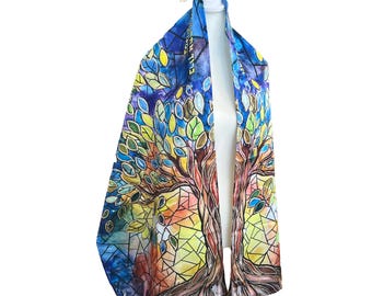 Può includere: Uno scialle di preghiera colorato con un disegno dell'albero della vita. Lo scialle presenta una vivace illustrazione ad acquerello di un albero con foglie nei toni del verde, blu e giallo. Lo sfondo ha un effetto vetrata con toni caldi.