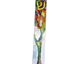 Può includere: Una mezuzah in legno con un dipinto ad acquerello di un albero con colori autunnali. La lettera ebraica Shin è dipinta in oro sulla mezuzah.