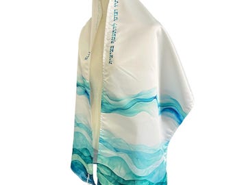 Può includere: Uno scialle da preghiera tallit bianco con un motivo a onde in stile acquerello nei toni del blu ottanio, turchese e blu intenso. L'atarah, o fascia per il collo, è ricamata con testo ebraico blu. Il capo presenta frange annodate bianche.
