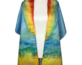 May include: A colorful prayer shawl with a watercolor design. The shawl features a gradient of colors, including blue, green, yellow, and red. Hebrew text is printed on the top edge. The shawl is draped over a mannequin.
