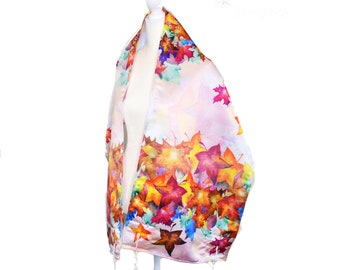 May include: A white silk tallit with a colorful autumn leaf print. The leaves are in shades of orange, red, yellow, and green. The tallit has white fringes.