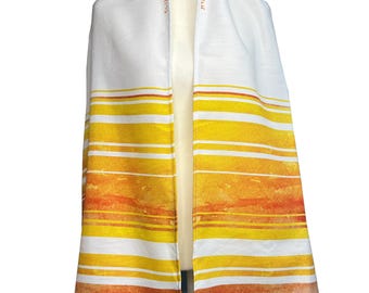 Può includere: Sciarpa da preghiera bianca con strisce orizzontali nelle tonalità del giallo, arancione e marrone. Lo scialle ha un effetto acquerello ed è drappeggiato su una testa di manichino bianca. I bordi sono rifiniti con nappe.