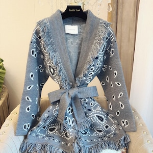 May include: A gray cardigan with a shawl collar, fringe trim, and a self-tie belt. The sweater features a white and black paisley pattern and the text "Double Yang" on the label.