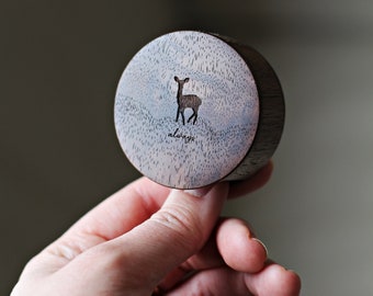 May include: A small wooden box with a light blue and gray design. The box has a deer silhouette and the word "always" engraved on the top.