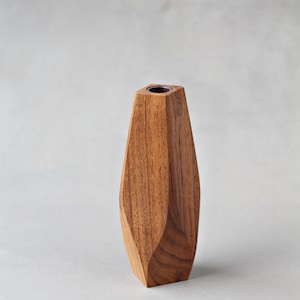 May include: A wooden vase with a geometric design. The vase is made of light brown wood and has a smooth finish.