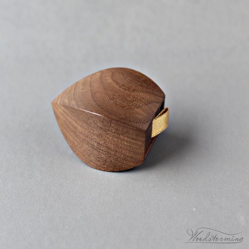 May include: A small, teardrop-shaped wooden ring box with a gold ribbon. The box is made of dark wood with a natural grain pattern.