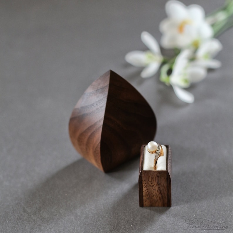Unique handmade ring box in shape of flower bud or water drop. Made of walnut wood, sanded especially smooth for a shiny look and smooth feel. 
Box opens by pulling gold color ribbon on the bottom of the box, pulling out small inner drawer for ring.
